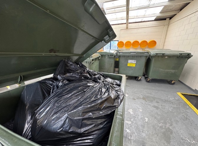 Sealed black bags of ship-generated quarantine waste inside a compliant collection bin at a port quarantine facility.