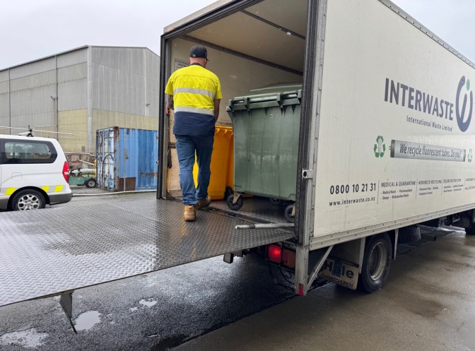 Quarantine waste collection truck being loaded with sealed bins by Interwaste operator at an international shipping port.