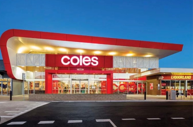 Exterior view of a Coles supermarket during dusk, featuring the store's name prominently displayed in red on the facade.